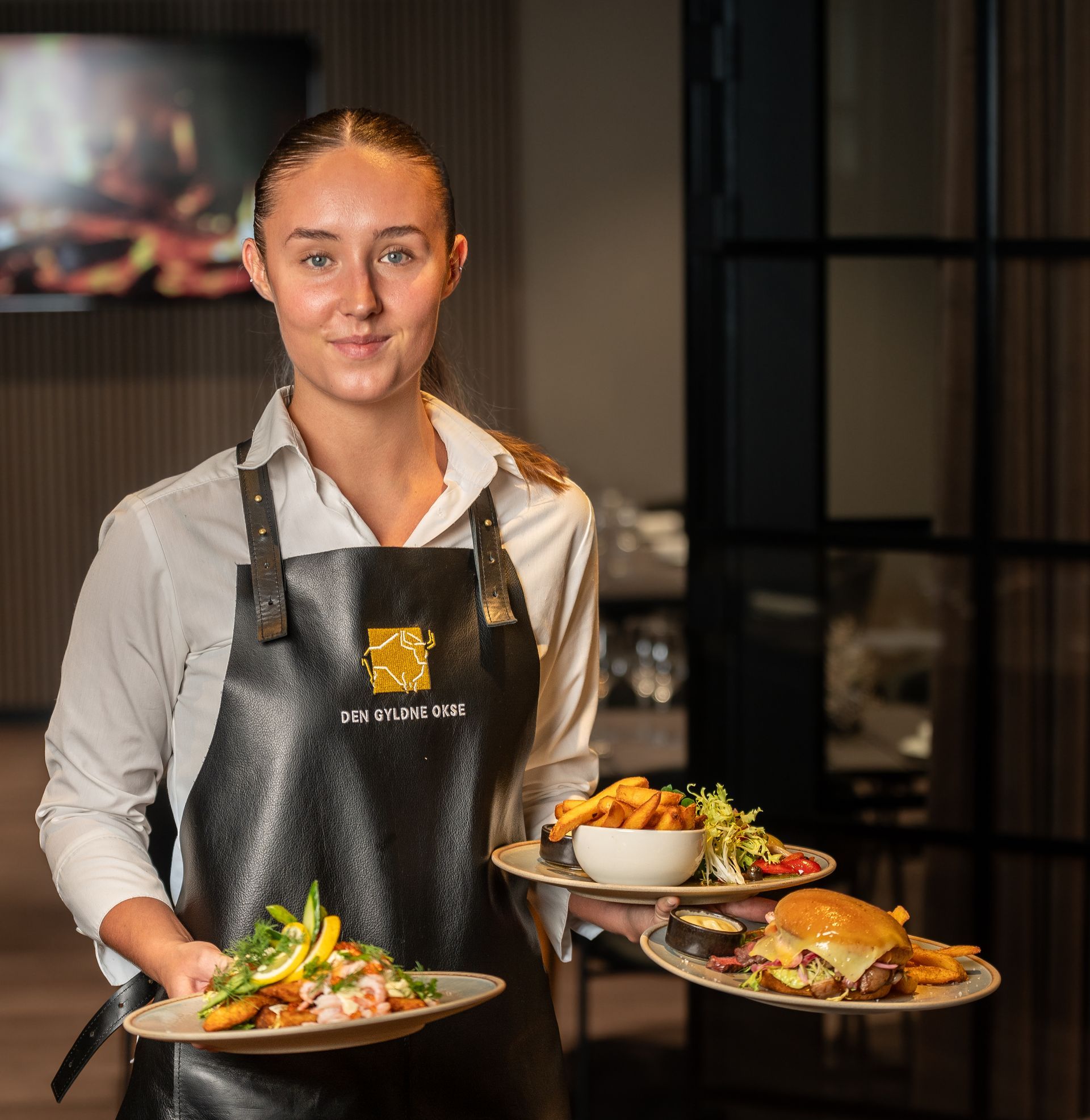 Servitrice holder tallerkener med mad på en restaurant; fisk, burger og pommes frites.
