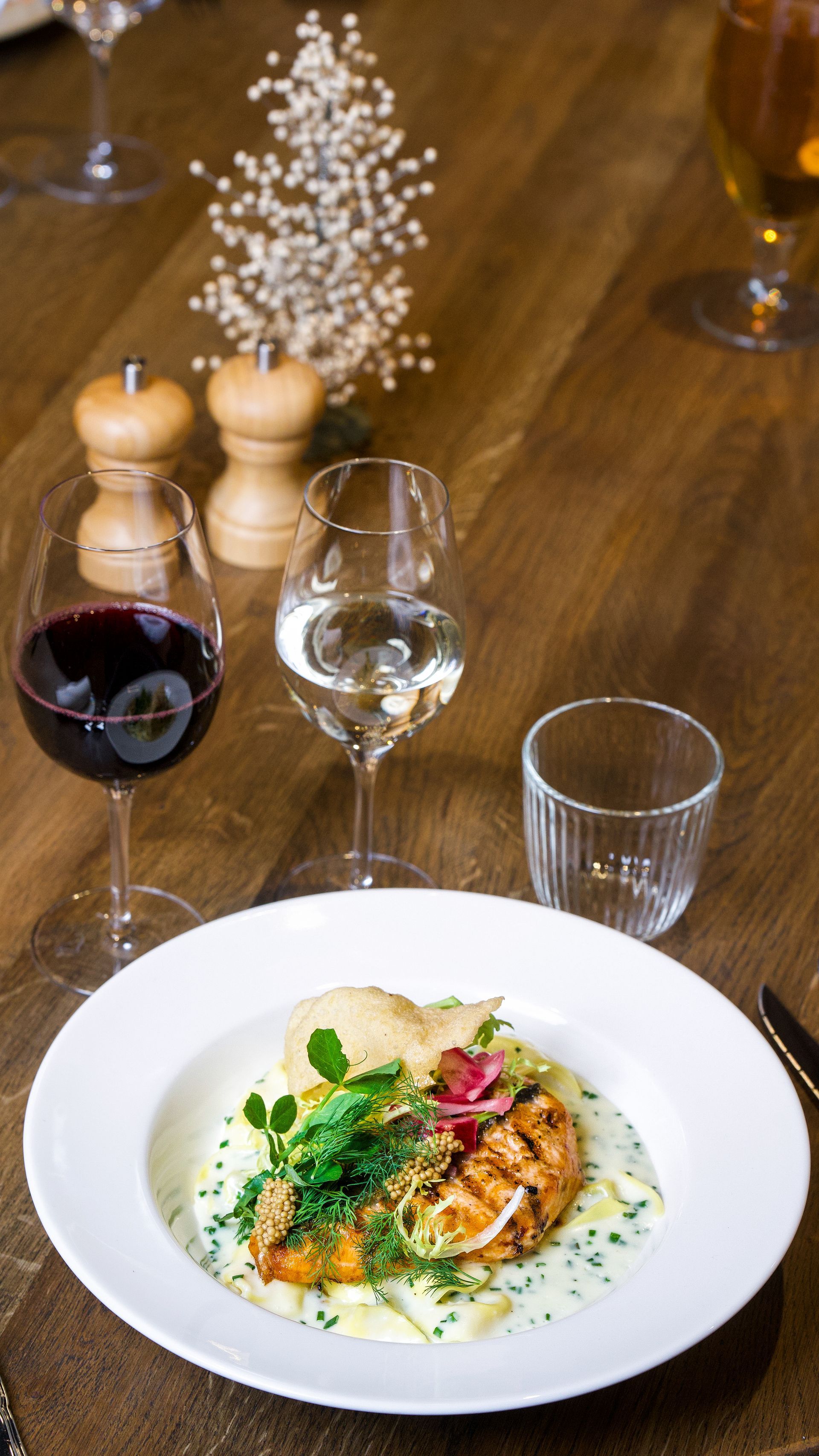 Grillet laks på kartoffelmos med vinglas, blomster og krydderier på et træbord.