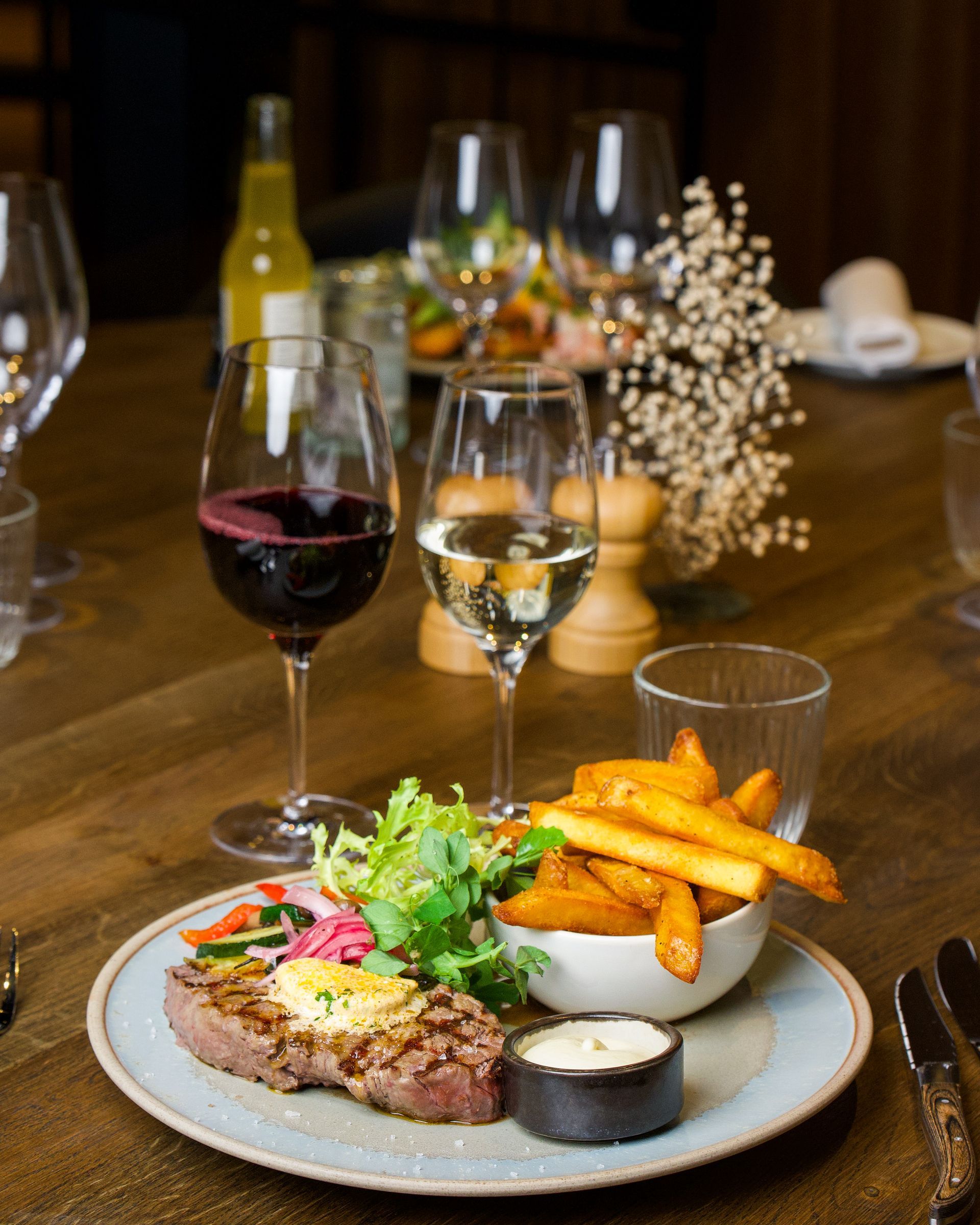 Bøfmiddag på træbord med rødvin, hvidvin og pommes frites.