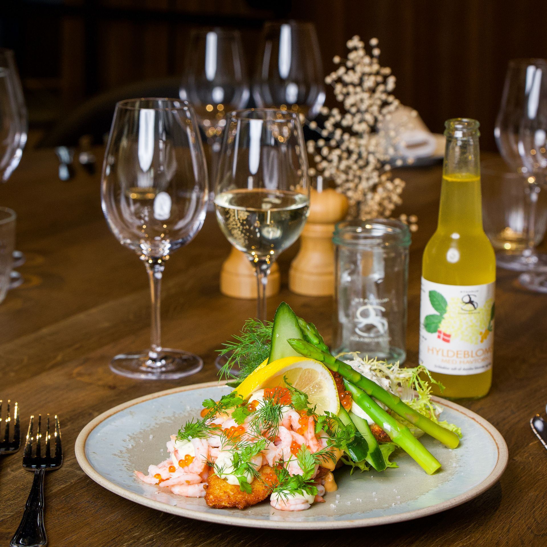Tallerken med rejeret med sidesalat, glas vin og en flaske sodavand på et træbord.