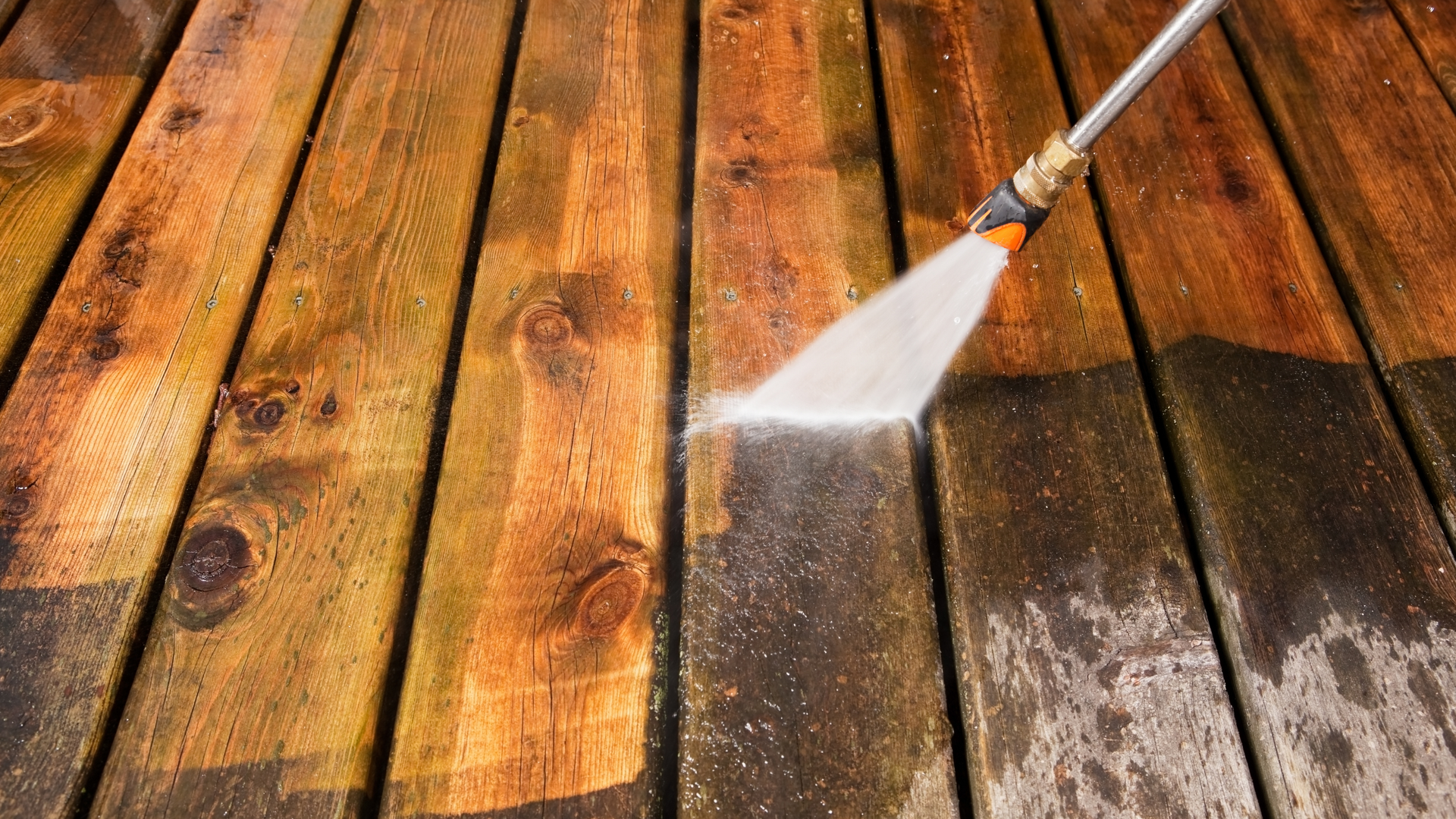 A person is cleaning a wooden deck with a high pressure washer.