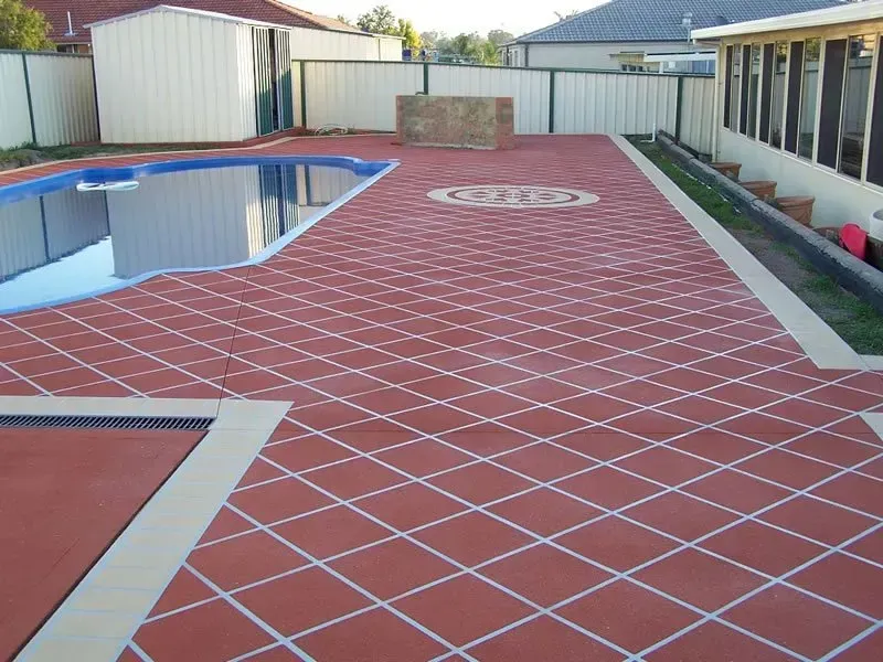 A swimming pool is surrounded by a red tiled floor — Concrete Colour Solutions in Morisset, NSW
