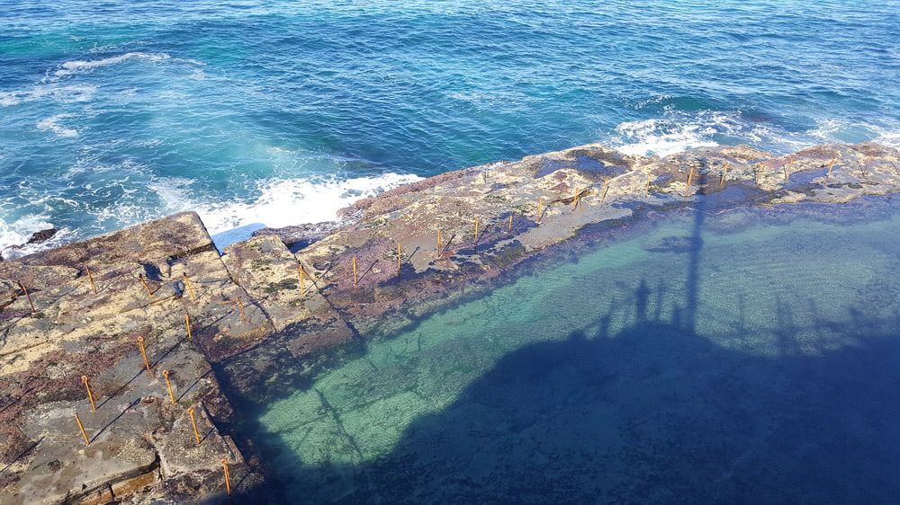 A Pool of Water Surrounded by Rocks Next to The Ocean — Concrete Colour Solutions in Morisset, NSW
