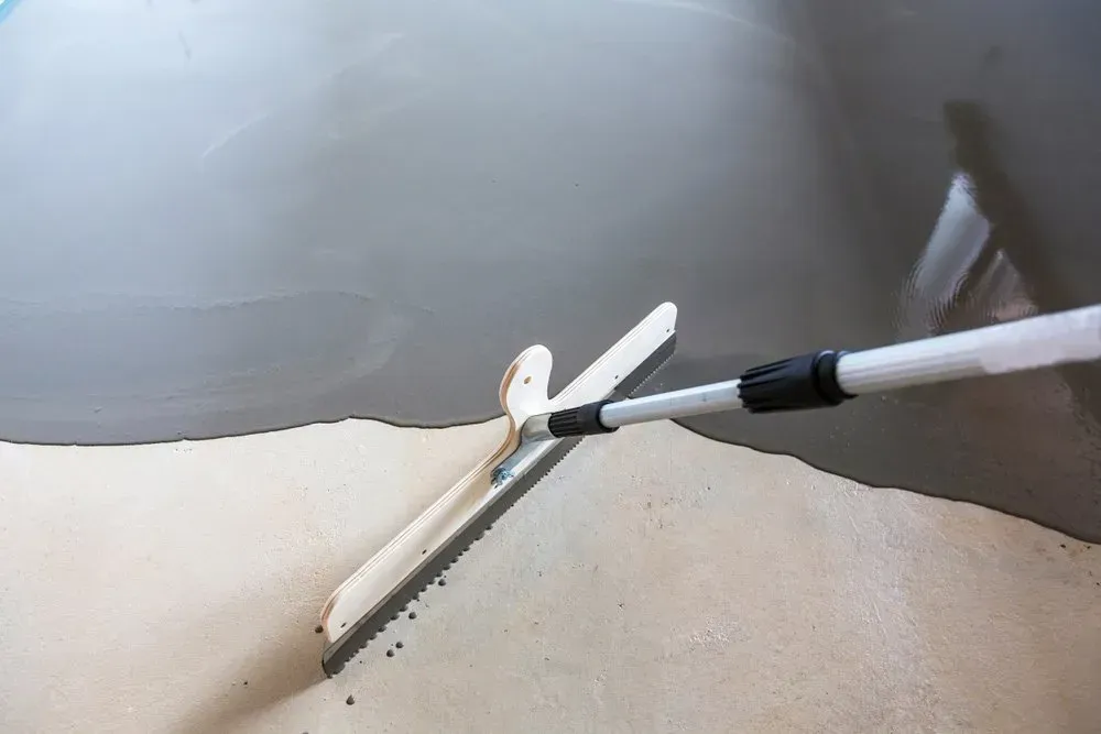 A Person Is Spreading Concrete on The Floor with A Trowel — Concrete Colour Solutions in Morisset, NSW