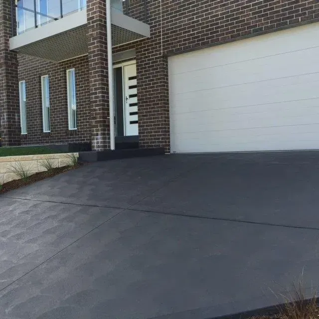 A brick house with a white garage door and a concrete driveway leading to it. — Concrete Colour Solutions in Morisset, NSW