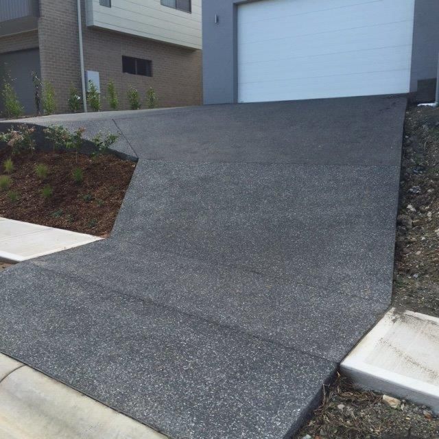 A concrete driveway leading to a garage with a white garage door — Concrete Colour Solutions in Morisset, NSW