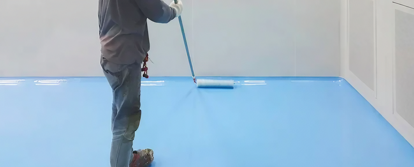 A Man Is Painting a Blue Floor with A Broom — Concrete Colour Solutions in Morisset, NSW