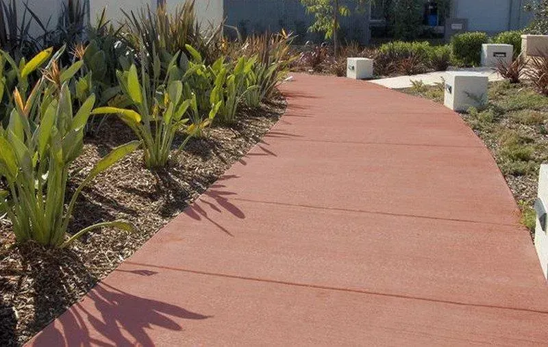 A red concrete walkway surrounded by plants and bushes — Concrete Colour Solutions in Morisset, NSW