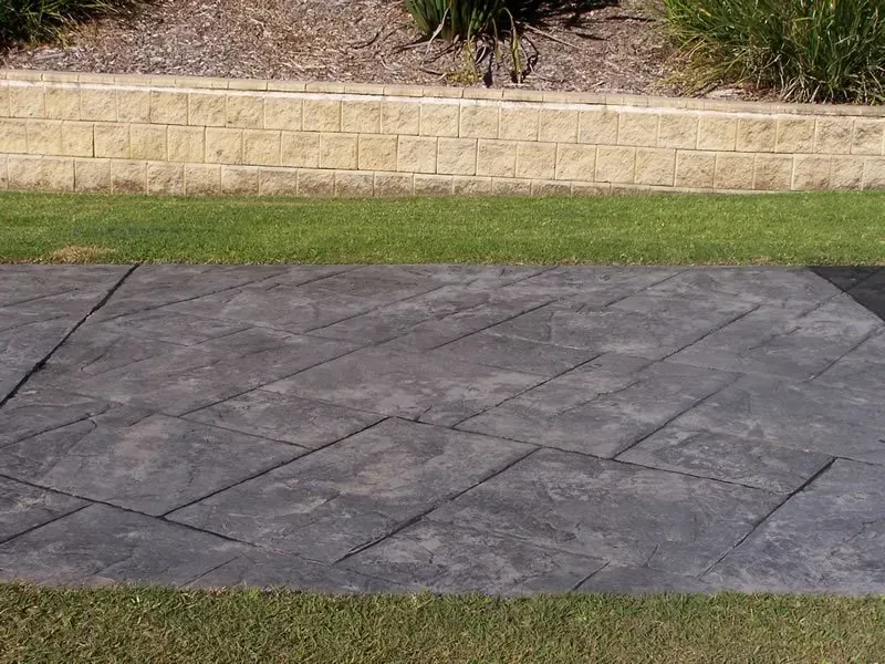 There is a brick wall in the background and a concrete walkway in the foreground. — Concrete Colour Solutions in Morisset, NSW