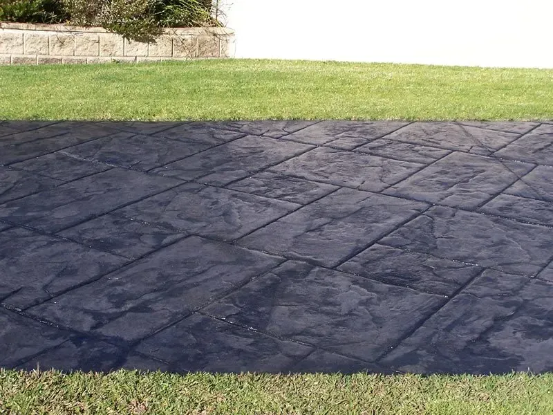 A black concrete patio is sitting in the middle of a lush green field. — Concrete Colour Solutions in Morisset, NSW