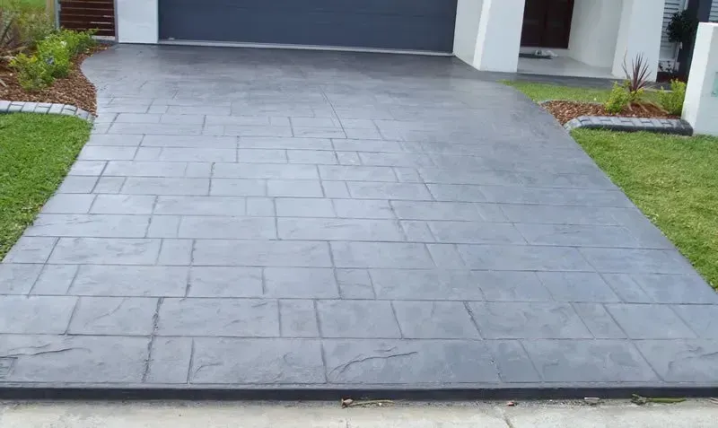 A concrete driveway leading to a house with a black garage door. — Concrete Colour Solutions in Morisset, NSW