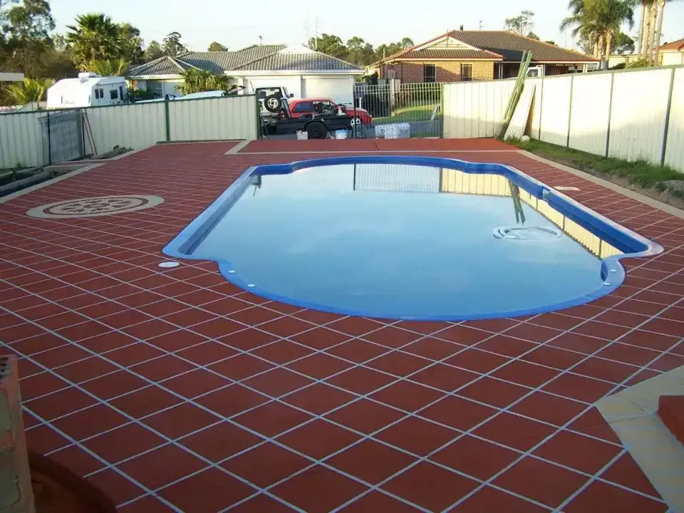 A Large Swimming Pool Is Surrounded by A Red Tiled Floor — Concrete Colour Solutions in Morisset, NSW