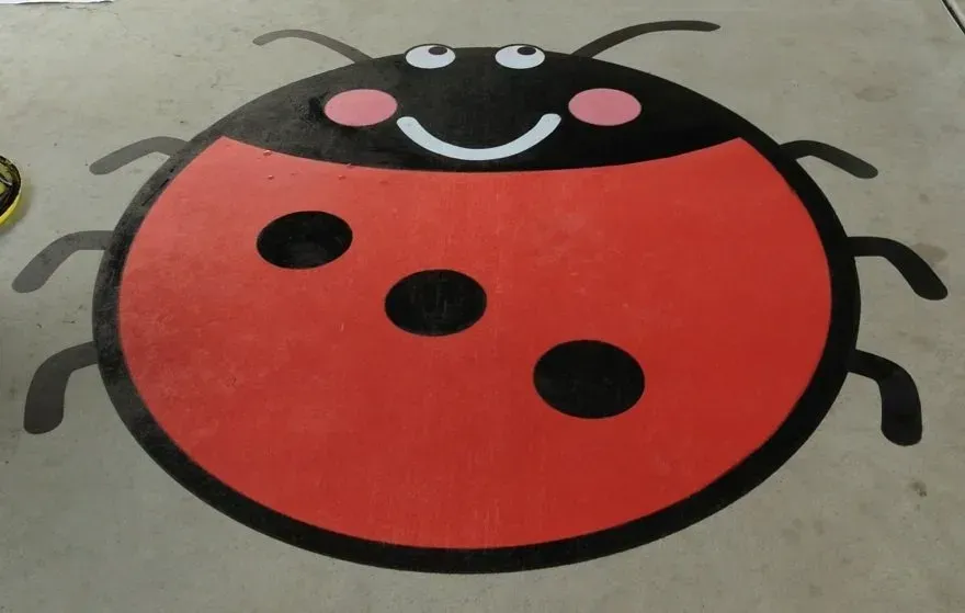 A ladybug with a smiling face is painted on the floor — Concrete Colour Solutions in Morisset, NSW
