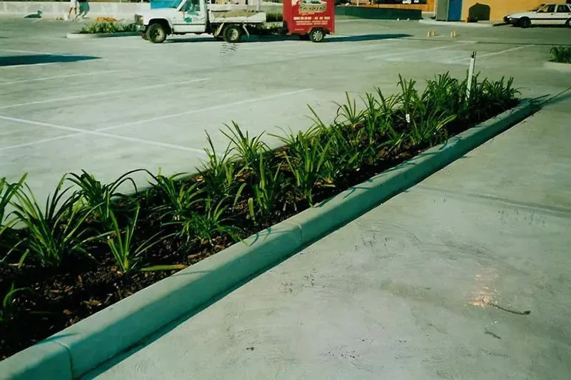 A red truck is parked in a parking lot next to a planter — Concrete Colour Solutions in Morisset, NSW