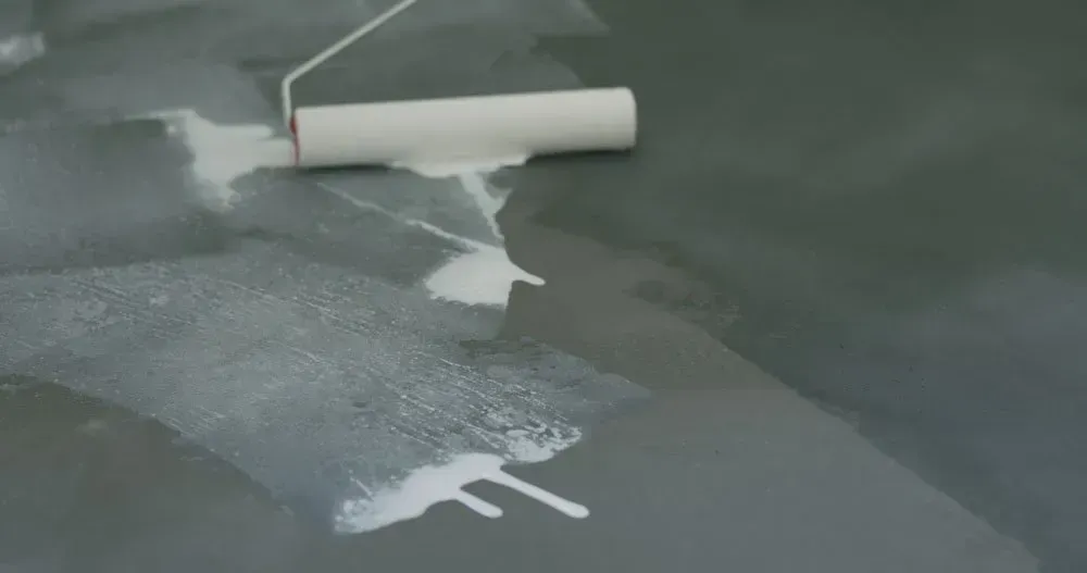 A Roller Is Being Used to Paint a Concrete Floor — Concrete Colour Solutions in Morisset, NSW