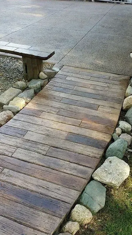A wooden walkway surrounded by rocks and a bench. — Concrete Colour Solutions in Morisset, NSW