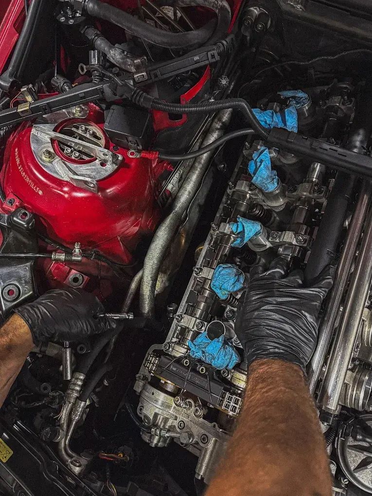 Hands wearing black gloves working on a red engine, blue-taped components, and metal parts. | Friendly Automotive