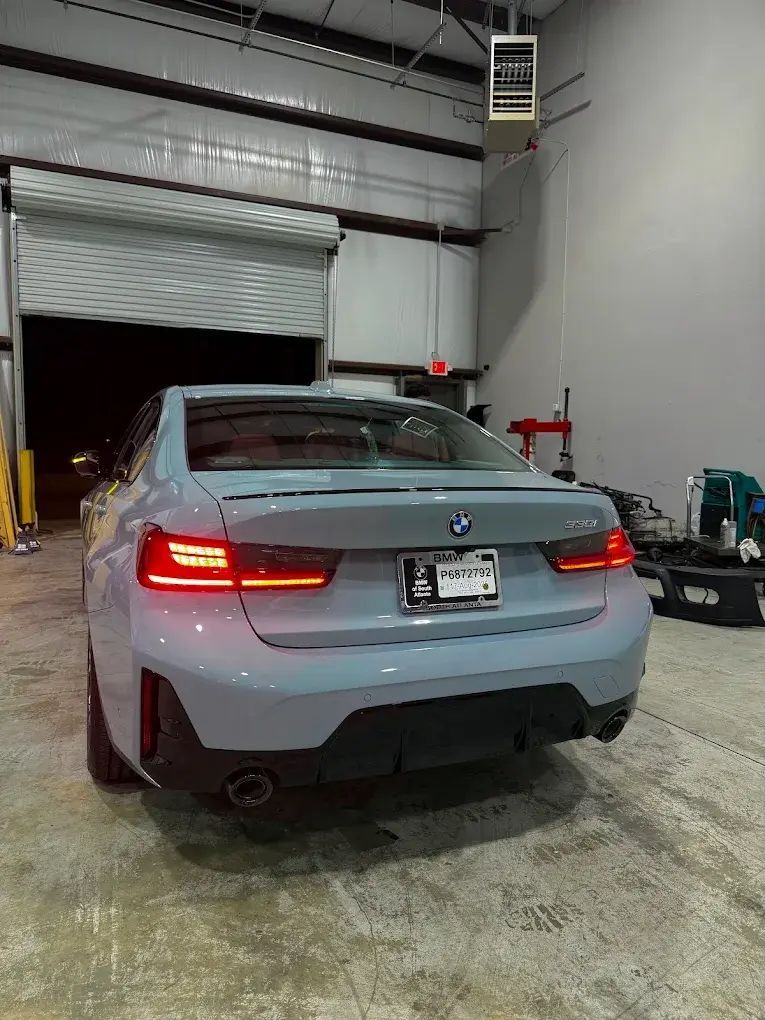 Gray BMW sedan parked in a garage with a rolling door open, red tail lights illuminated. | Friendly Automotive
