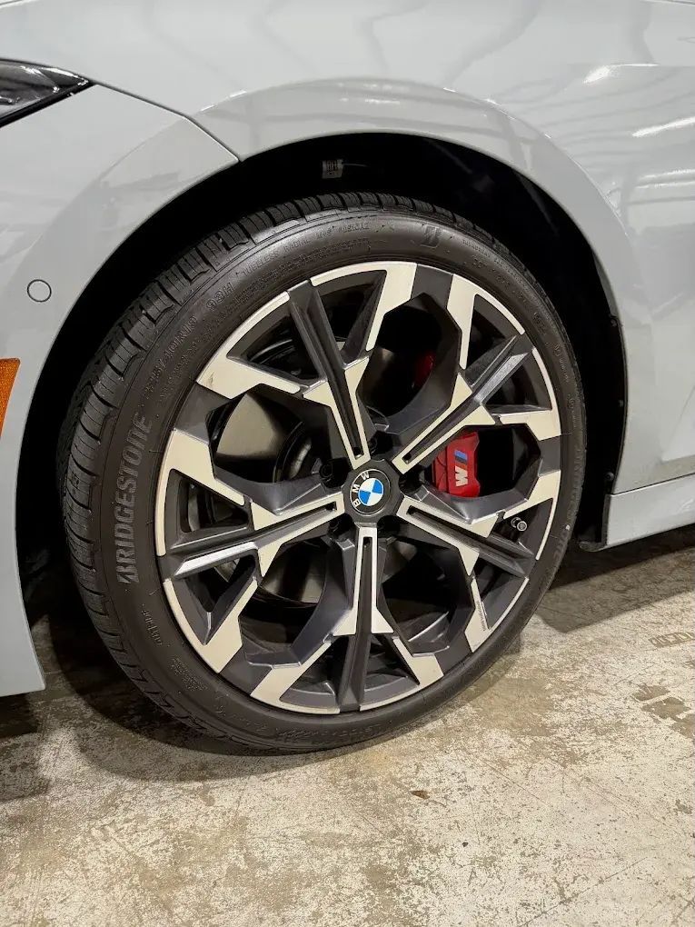 Gray car wheel with a black and silver rim, red brake caliper, and Bridgestone tire. | Friendly Automotive