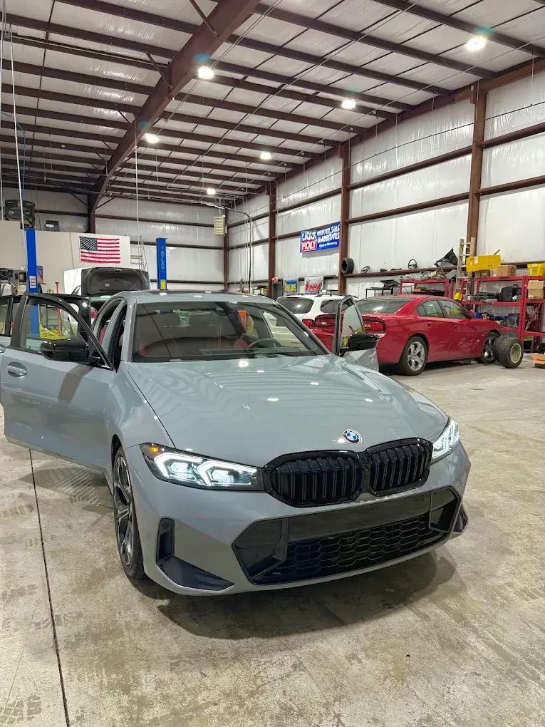 Gray BMW sedan in a garage with open door, black grill, and red car in the background. | Friendly Automotive