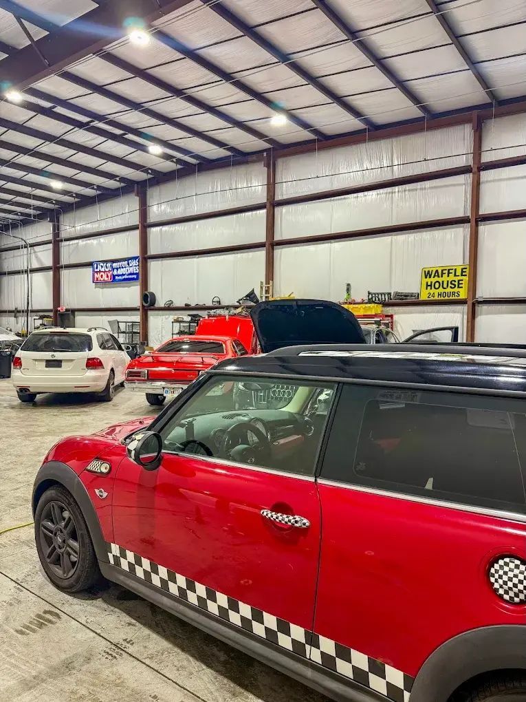 Red Mini Cooper in a garage, with other vehicles. A 