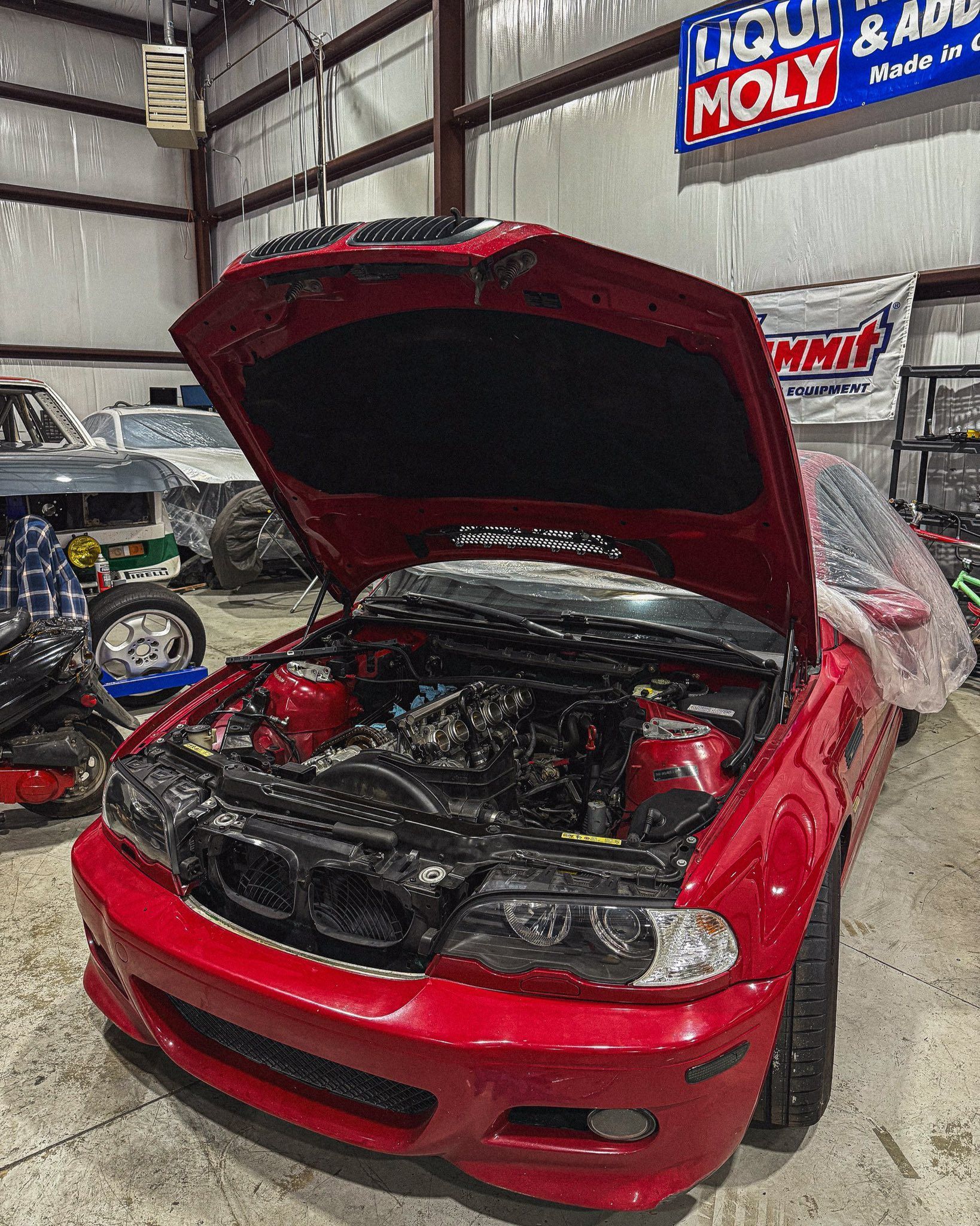 Red BMW with open hood in a garage, under repair. | Friendly Automotive