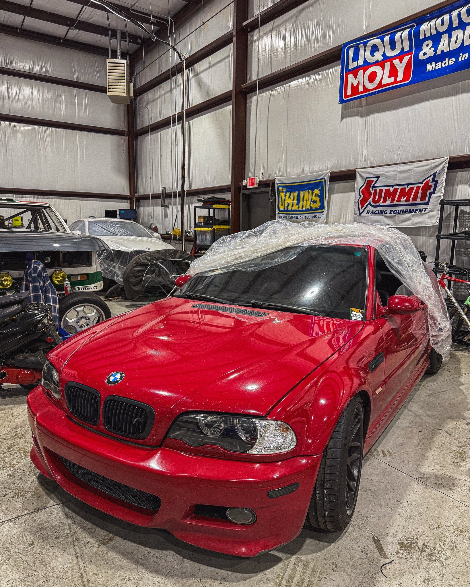 Red BMW sports car in a garage, covered partially in plastic wrap. | Friendly Automotive