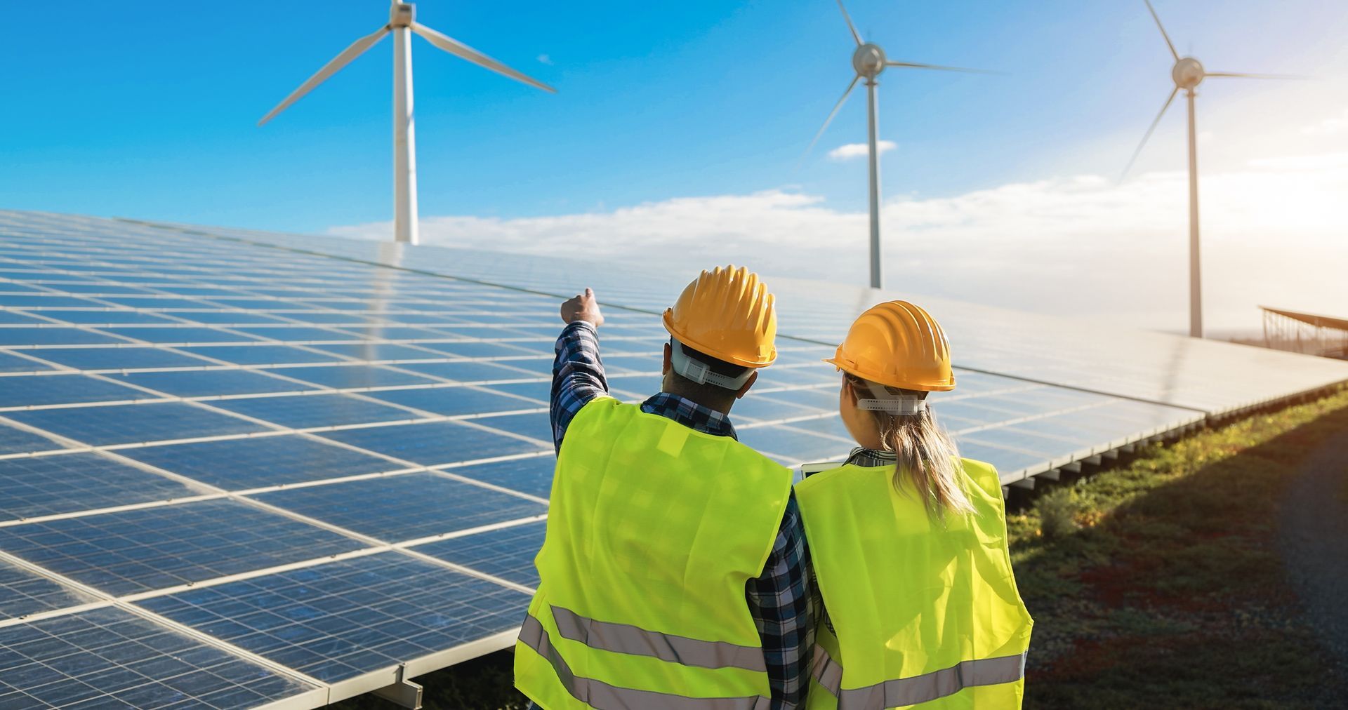 A man and a woman are standing in front of a solar panel and wind turbine.