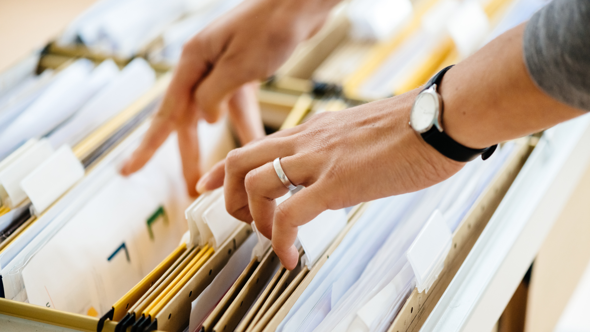 A person wearing a watch is looking through a filing cabinet.