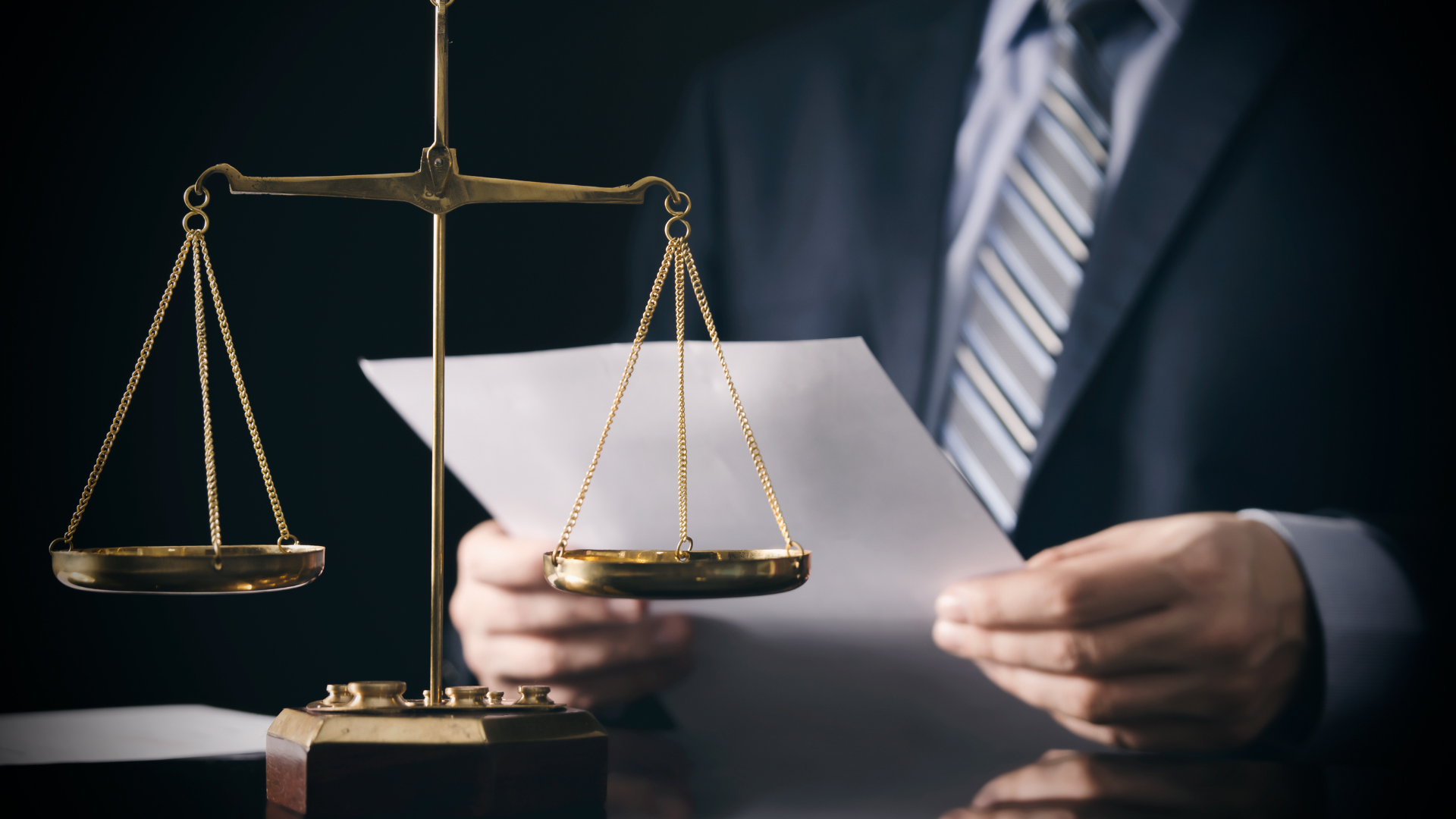 A man in a suit and tie is holding a piece of paper in front of a scale of justice.