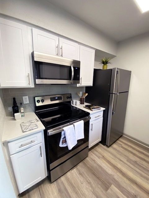 Modern apartment kitchen with white cabinets, stainless steel stove, microwave, and fridge.