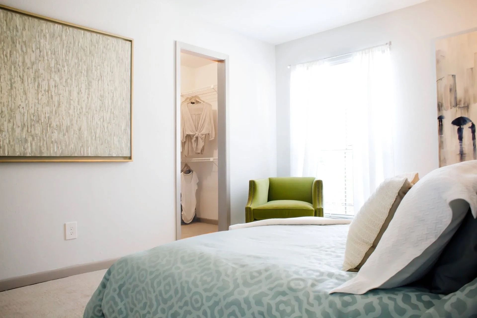 Bedroom with bed in foreground, green armchair by a bright window, and an open closet.