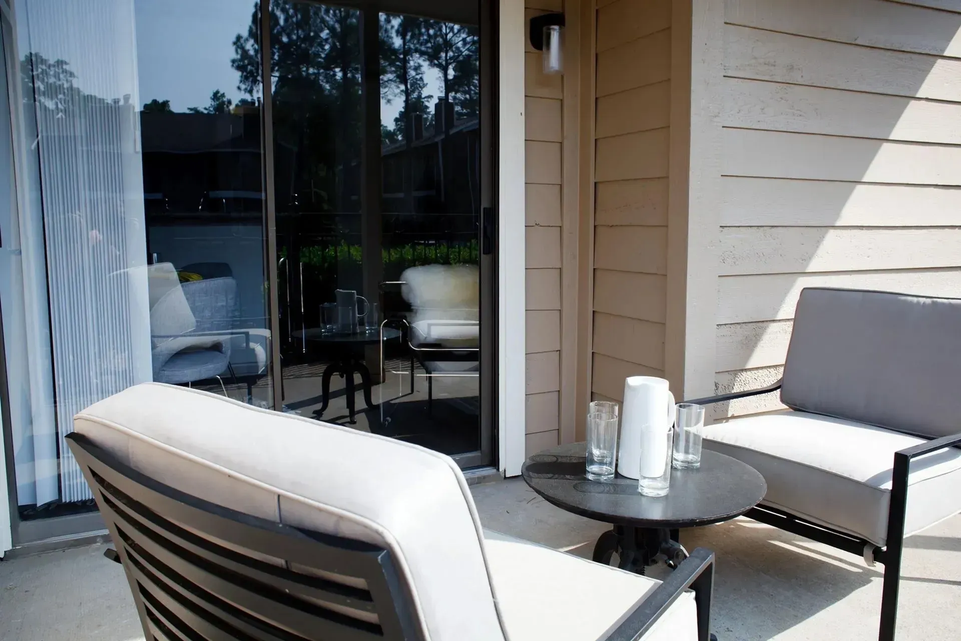 Patio with outdoor furniture set, glass table, sliding door, light tan siding.