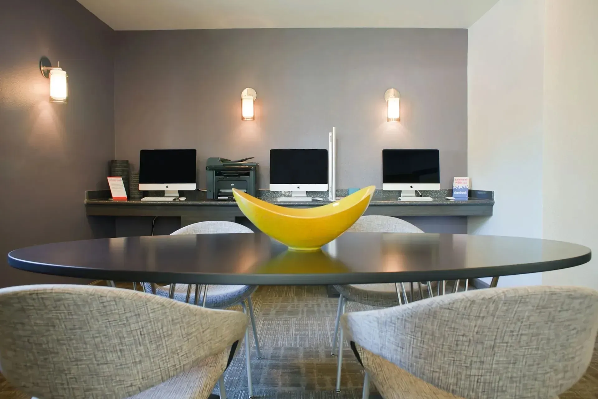 Office area with computers, printer, table, and chairs; a yellow bowl is on the table.