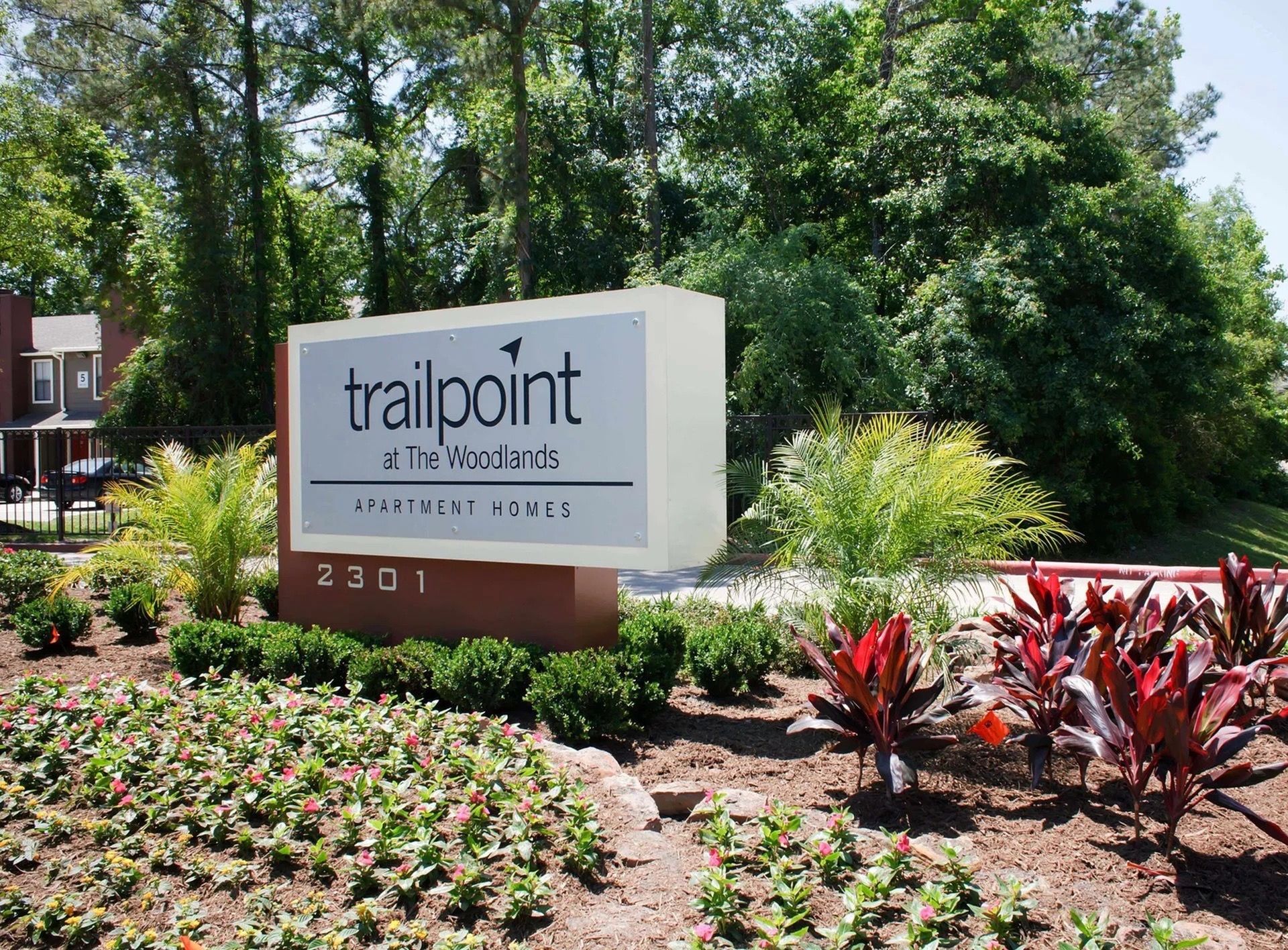 Exterior entrance sign for Trailpoint at The Woodlands apartment community with landscaping.