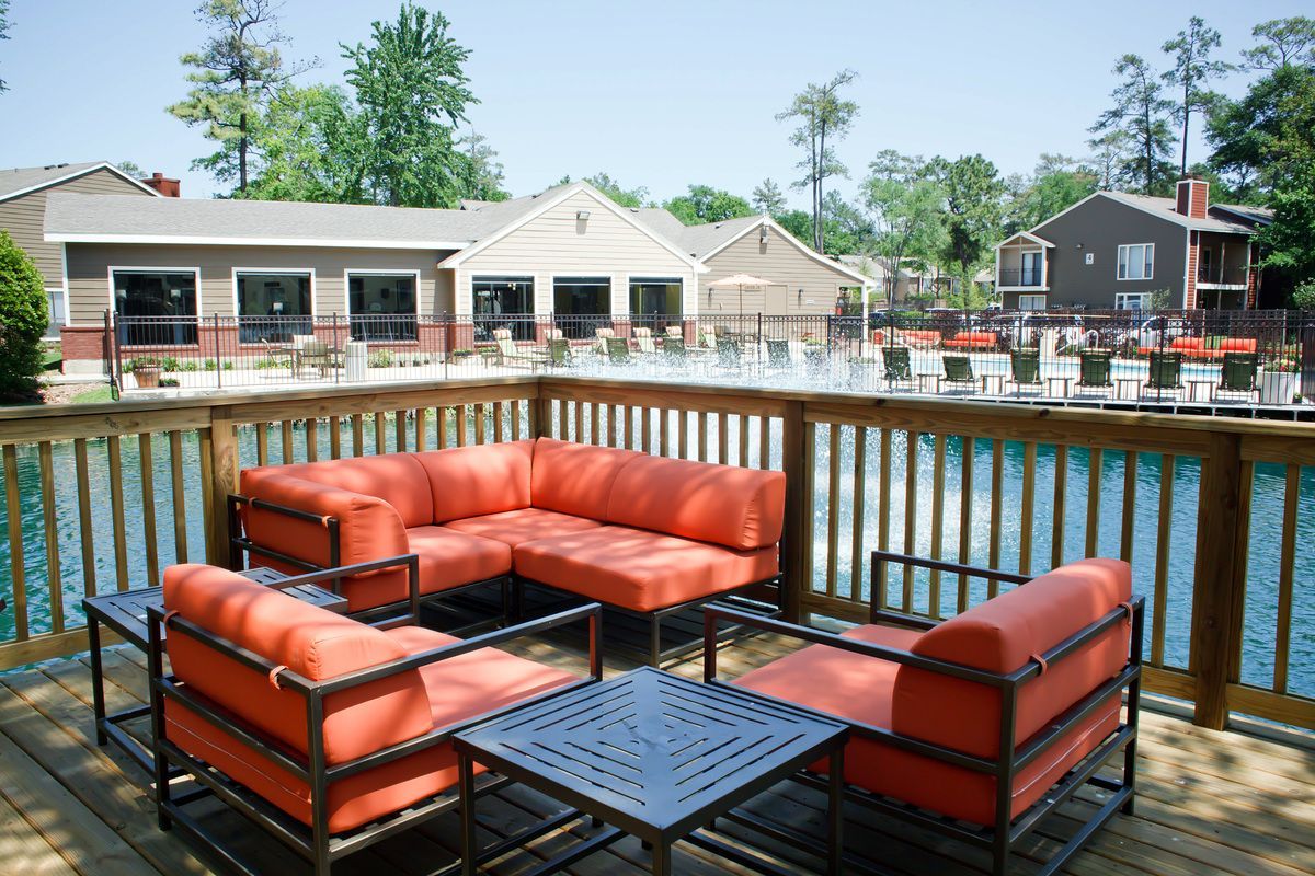 Outdoor patio with orange furniture on a wooden deck overlooking a lake with buildings in the background.