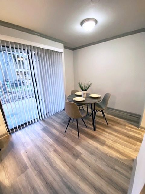 Dining area with round table, four chairs, and a sliding glass door with vertical blinds.