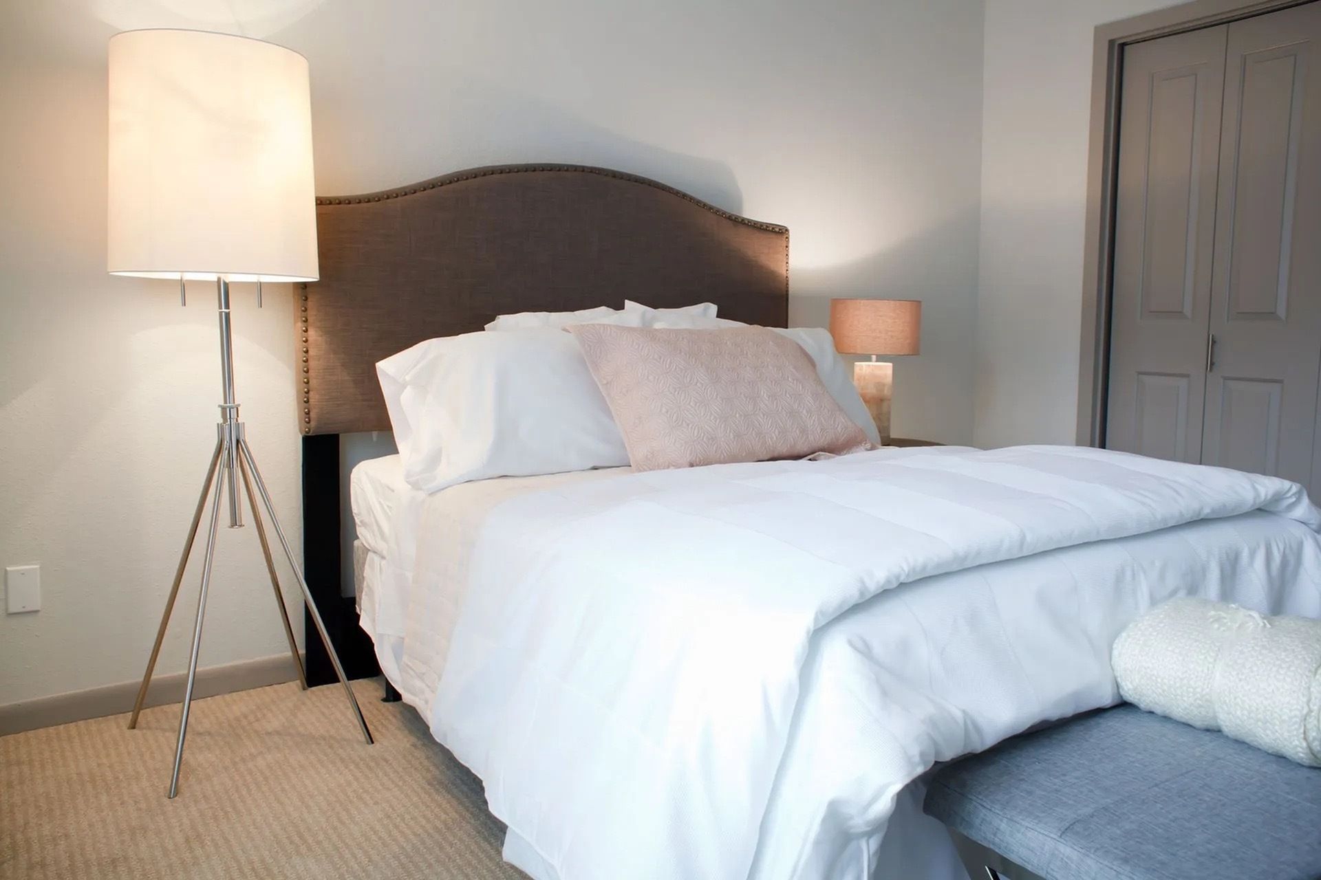 Bedroom with a large upholstered headboard bed, white bedding, and two lamps.