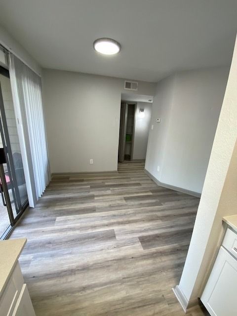 Empty apartment living area with wood-look flooring and sliding balcony door.