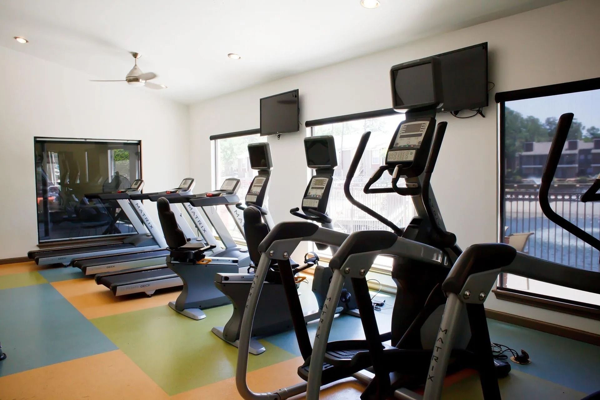 Community fitness center with treadmills, ellipticals, and wall-mounted TVs.