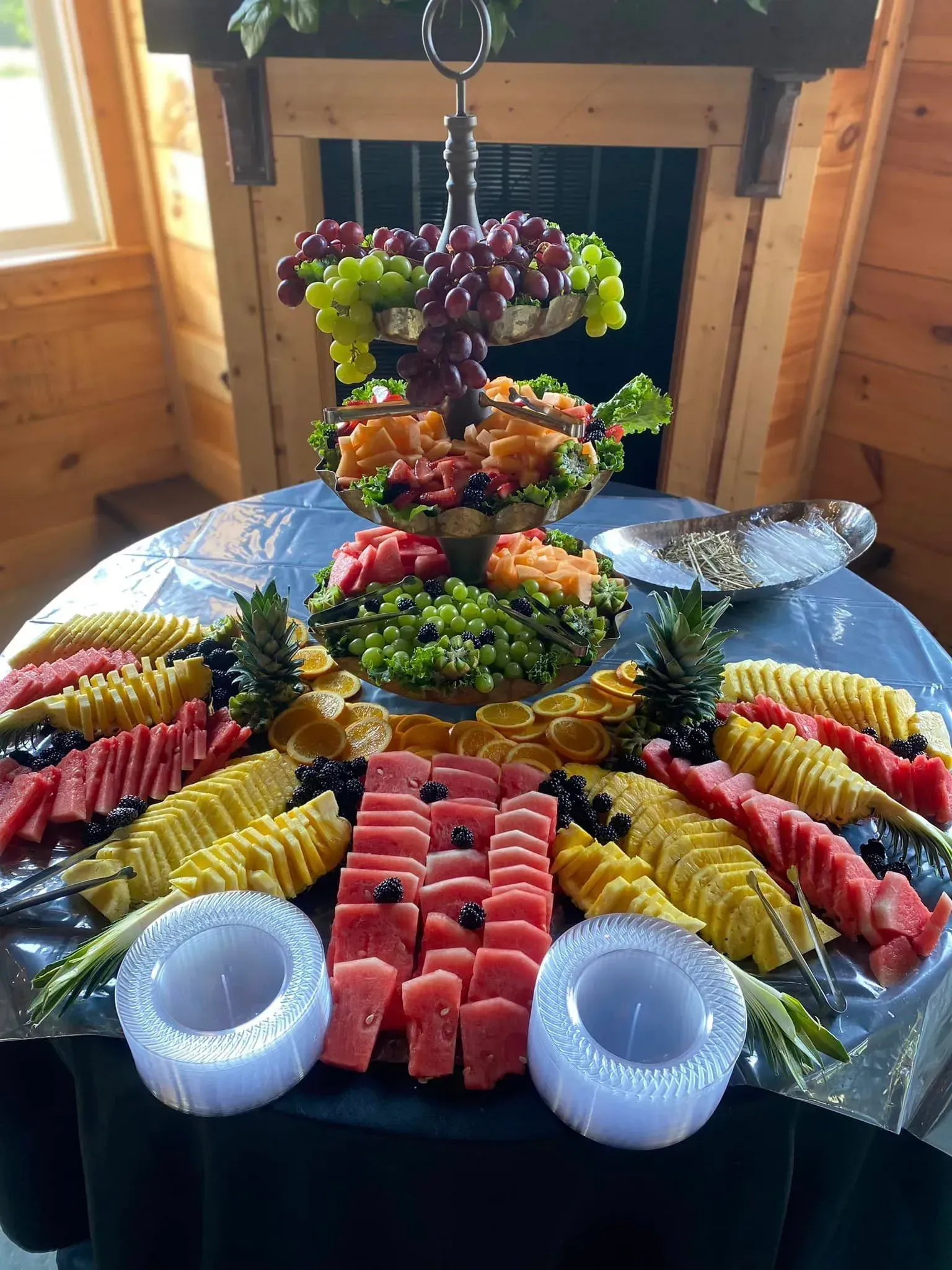 Colorful fruit and vegetable platter arranged on a table in a wooden room, with watermelon, grapes, and pineapple.