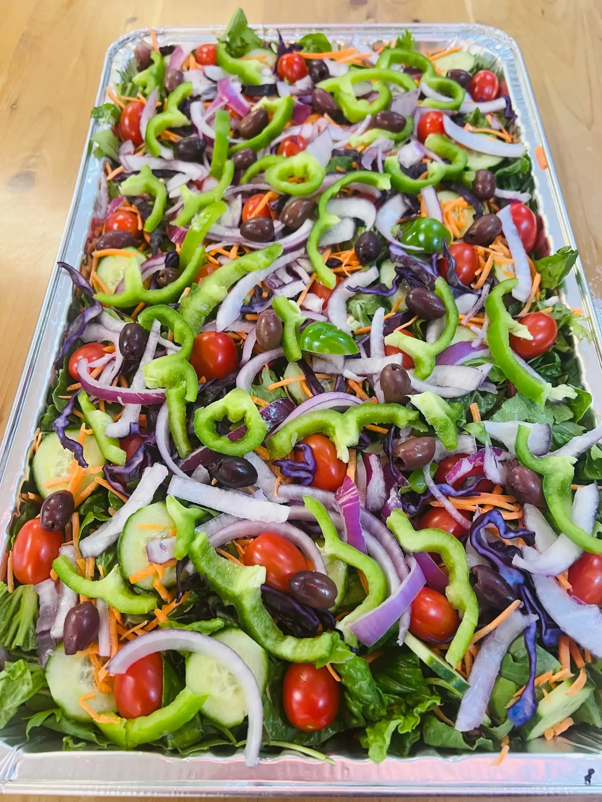 Tray of vegetable salad topped with cherry tomatoes, green peppers, purple onions, and black olives