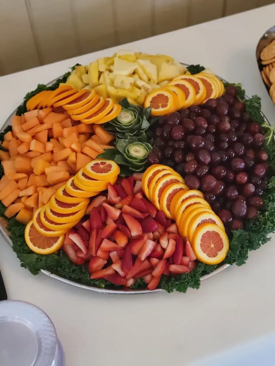 Fruit platter with orange slices, grapes, strawberries, melon, and pineapple arranged on a white tray