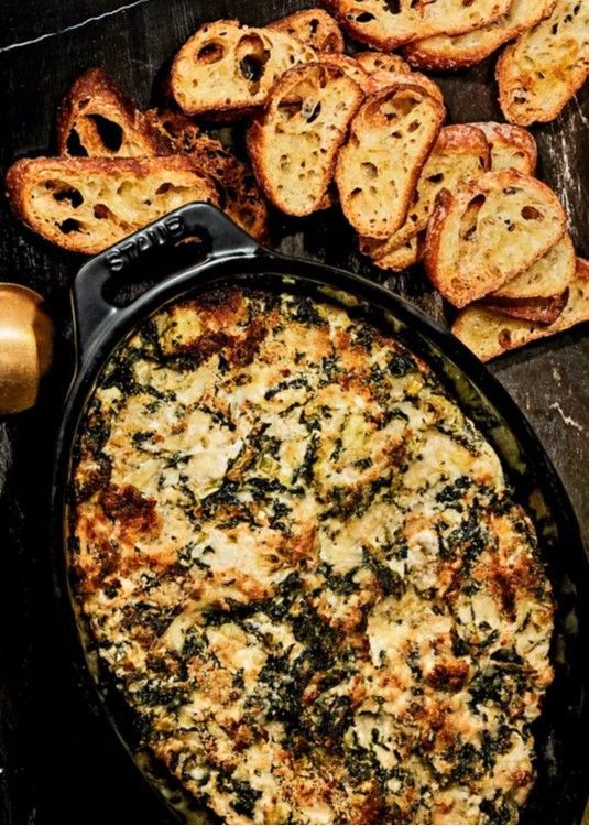 Baked spinach artichoke dip in a skillet, surrounded by toasted baguette slices