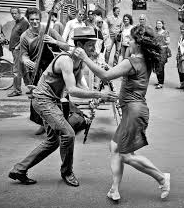 A man and a woman are dancing on the street in a black and white photo.
