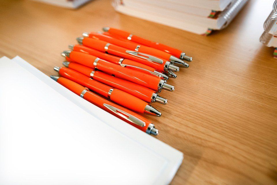 orange color pen  along notebooks on wooden table.