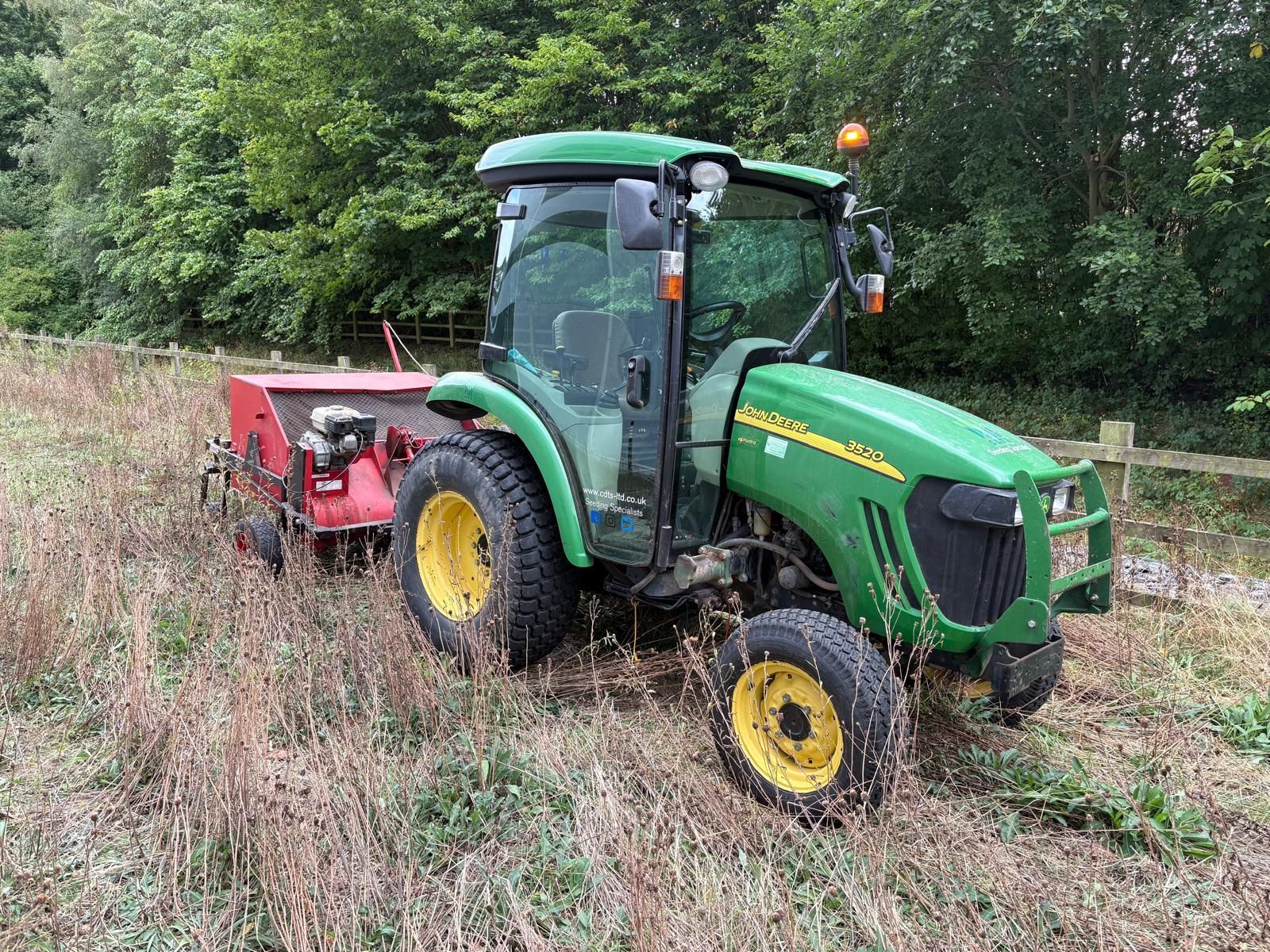  Compact tractor fitted with brush seed harvesting attachment operating in a meadow habitat