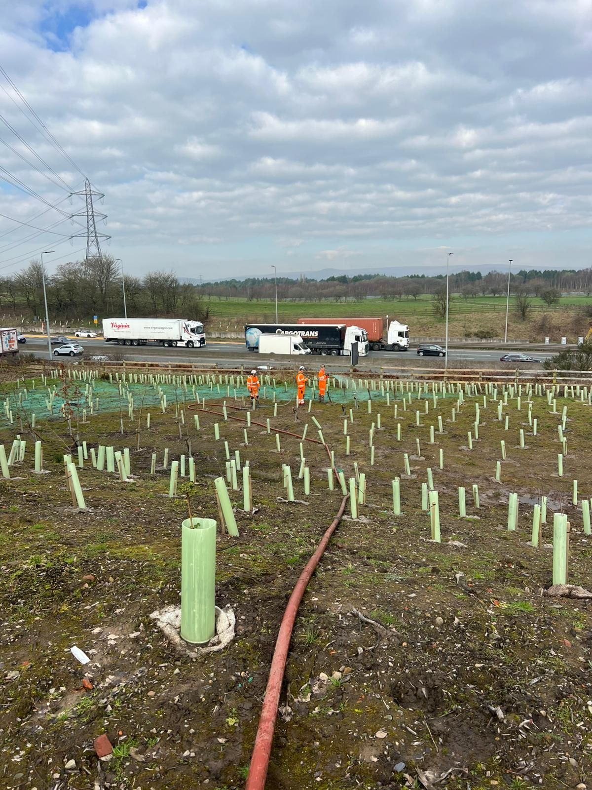 Person spraying liquid on a muddy field with wind turbines in the background