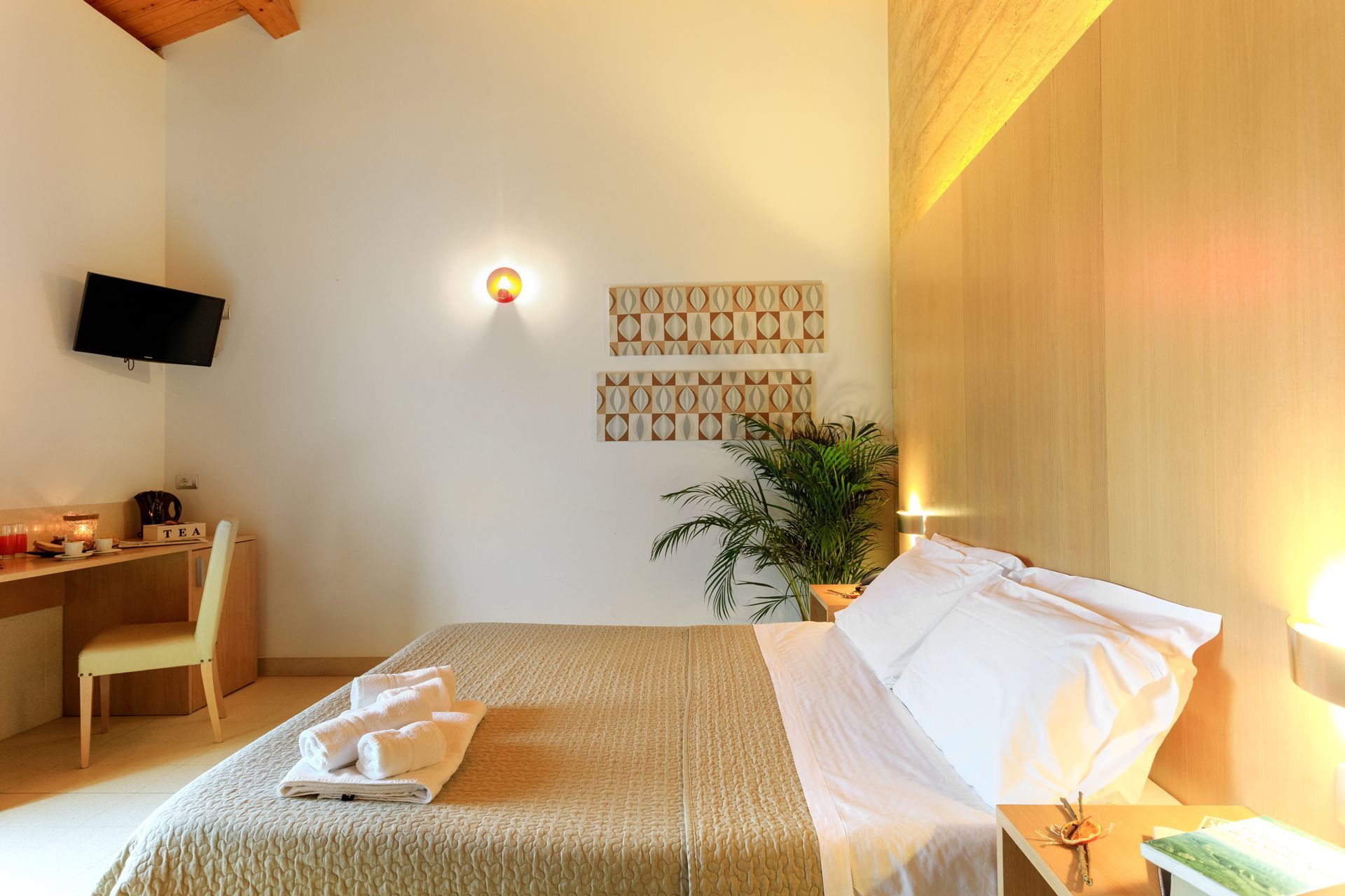 Luminosa camera d'albergo con letto ben rifatto, scrivania in legno, quadri alle pareti e luci calde.