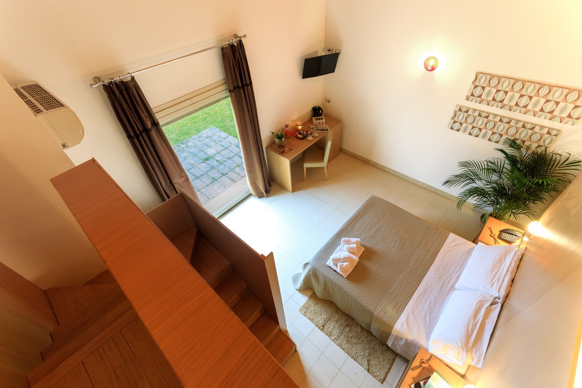 Luminosa camera da letto mansardata con letto, scrivania, finestra, scala e illuminazione calda.